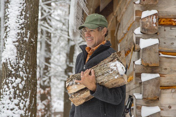 Mixed race man carrying firewood near snowy shed