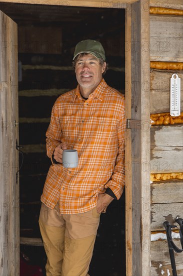 Mixed race man drinking coffee in log cabin doorway