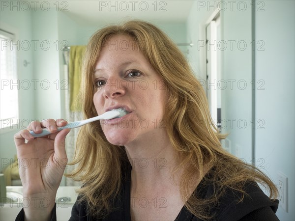 Caucasian woman brushing her teeth in bathroom