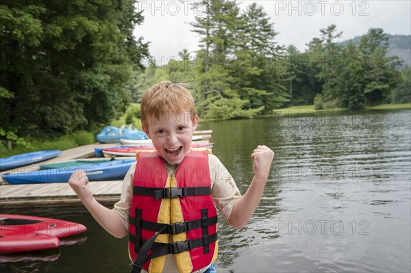 Caucasian boy wearing lifejacket by lake