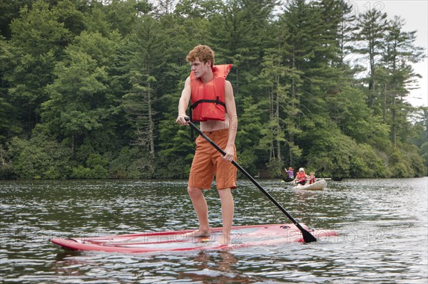 Caucasian teenage boy rowing paddleboat in lake