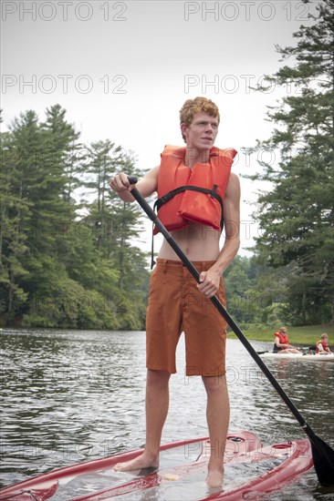 Caucasian teenage boy rowing paddleboat in lake