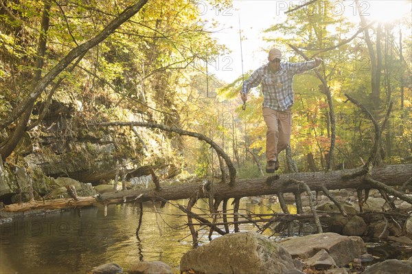 Caucasian man balancing on fallen tree over stream