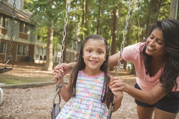 Hispanic mother pushing daughter in playground swing