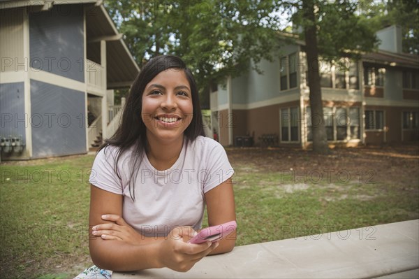 Smiling Hispanic girl holding cell phone near apartments