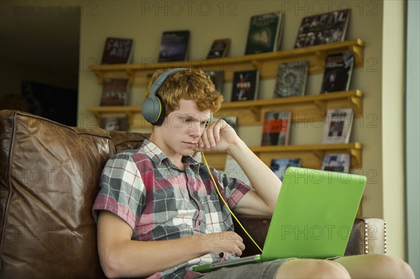 Caucasian boy sitting on sofa listening to laptop with headphones