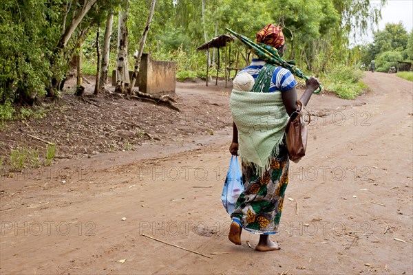 Mother carrying baby with traditional wrap on dirt road