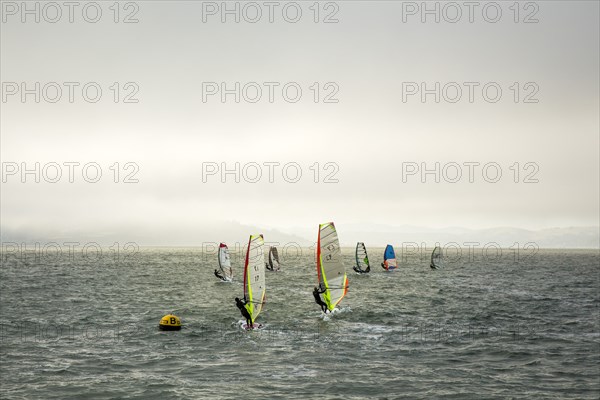 Windsurfers on ocean under cloudy sky