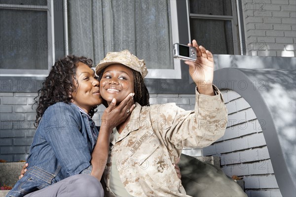 Black mother taking self-portrait with soldier daughter