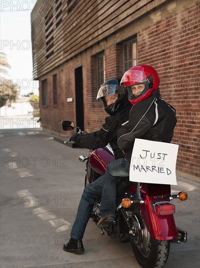 Caucasian couple riding on motorcycle with Just Married sign