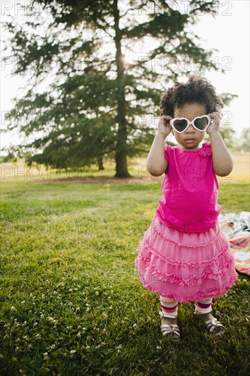 Black baby girl putting on sunglasses in park