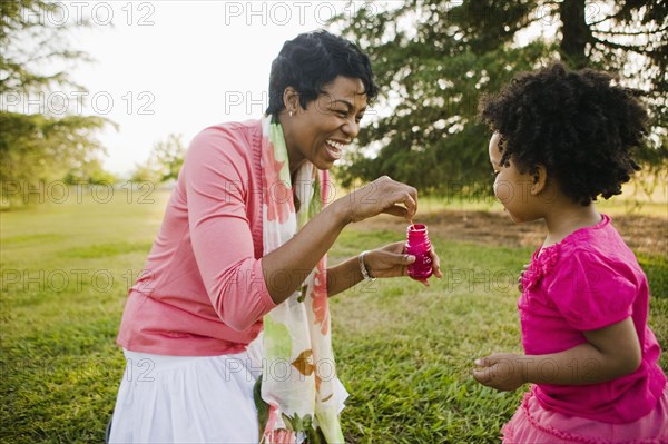Black mother and daughter blowing bubbles in park