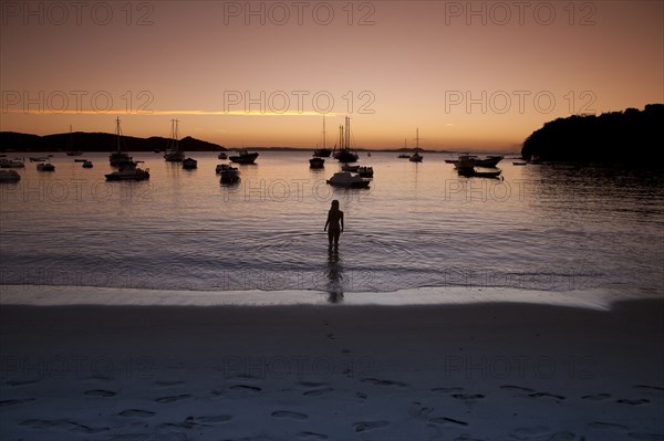 Young man wading in water at sunset