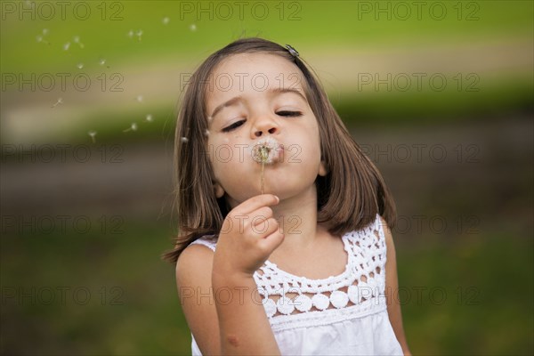 Mixed race girl blowing dandelion seeds