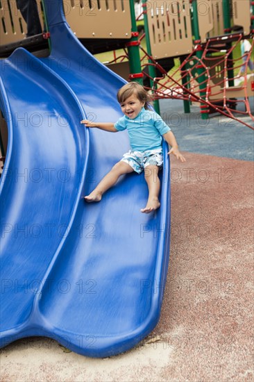 Mixed race boy sliding down slide in playground