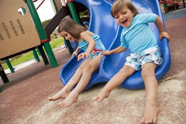 Brother and sister sliding down slide on playground