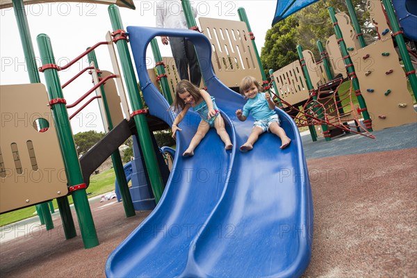 Brother and sister sliding down slide on playground