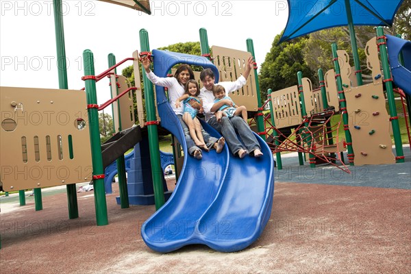 Family sliding down slide on playground