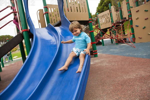 Mixed race boy sliding down slide on playground