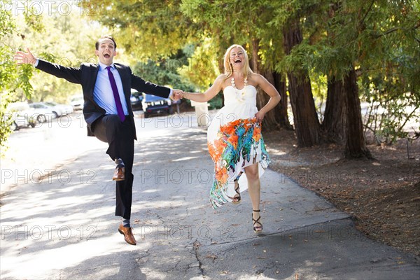 Caucasian newlywed couple skipping on road