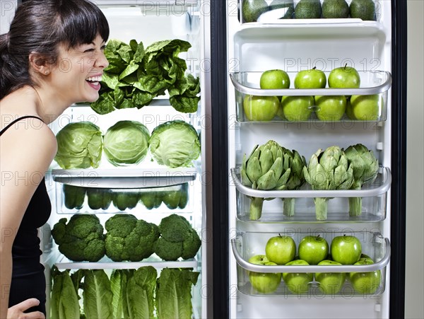 Mixed race woman looking at green vegetables in refrigerator