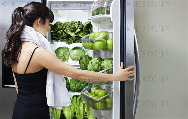 Mixed race woman looking at green vegetables in refrigerator