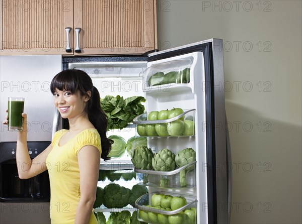 Mixed race woman drinking healthy drink near refrigerator