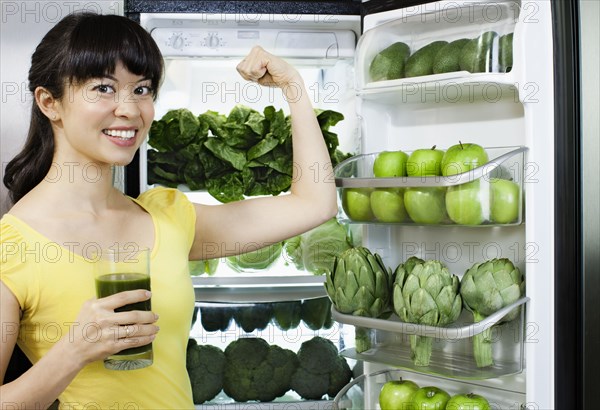 Mixed race woman drinking healthy drink near refrigerator