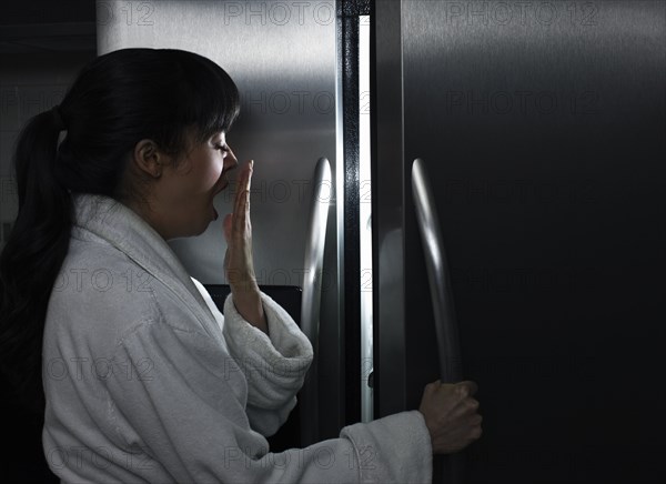 Sleepy mixed race woman looking in refrigerator at night