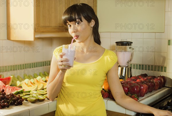 Mixed race woman drinking smoothie in kitchen