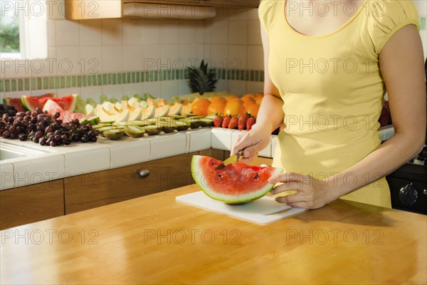 Mixed race woman cutting watermelon in kitchen