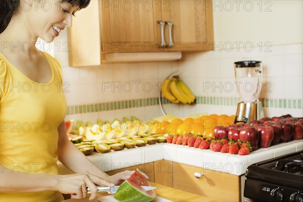 Mixed race woman cutting watermelon in kitchen