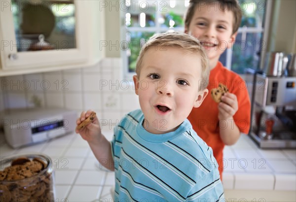Caucasian brothers sneaking cookies in kitchen