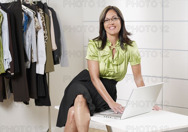 Hispanic businesswoman working on laptop in boutique