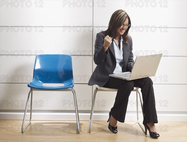 Hispanic businesswoman using laptop in waiting room