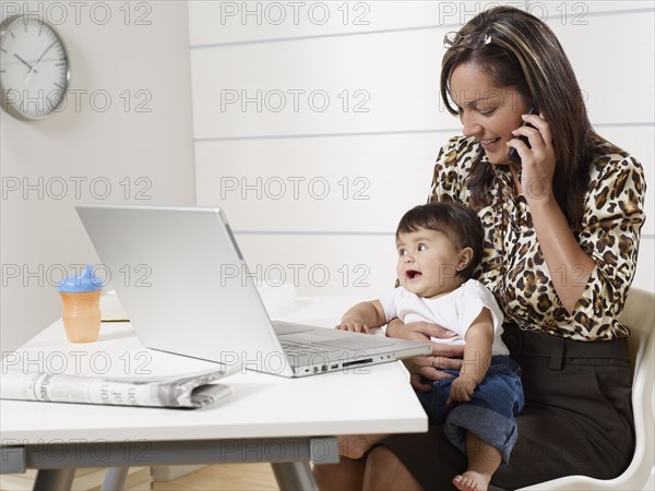 Hispanic working mother holding baby son and talking on phone