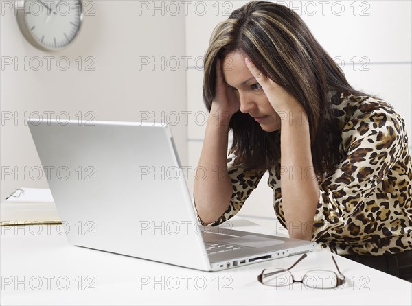 Hispanic businesswoman looking at laptop with head in hands