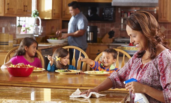Mother cleaning while children eat in background