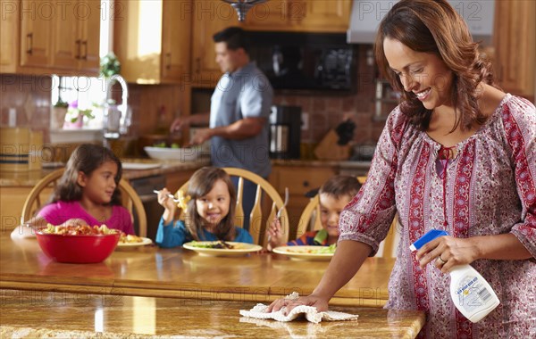 Mother cleaning while children eat in background