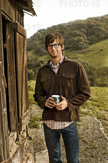 Caucasian man holding cup of coffee by barn