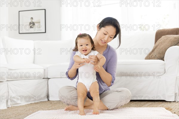 Mother helping baby girl stand in living room