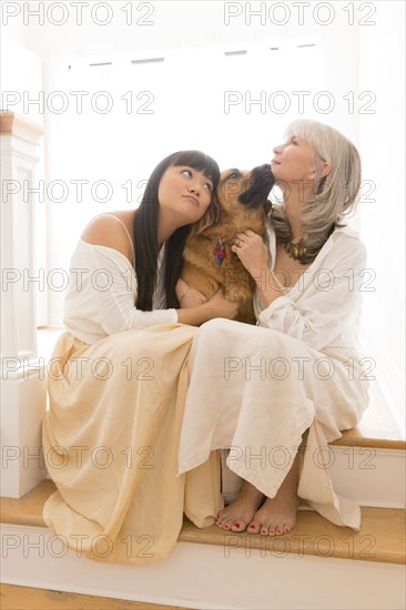 Mother and daughter hugging dog on steps