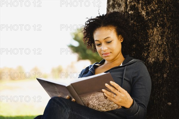 African woman holding book under tree