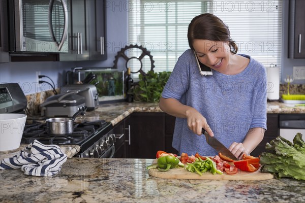 Mixed race woman talking on phone and chopping vegetables