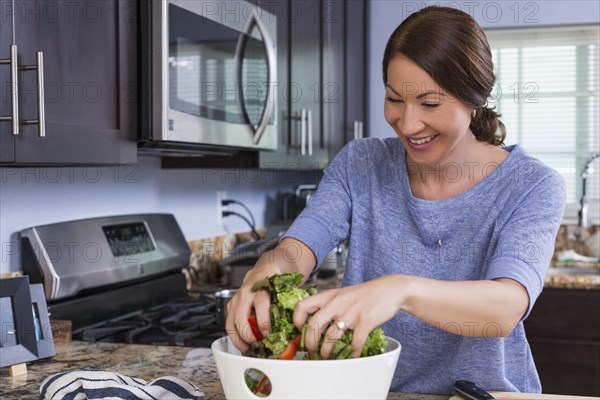 Mixed race woman tossing salad in kitchen