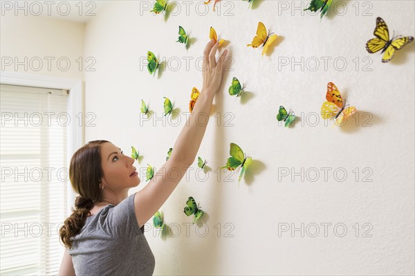 Mixed race woman decorating wall with butterflies