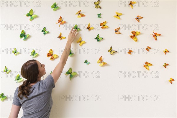 Mixed race woman decorating wall with butterflies