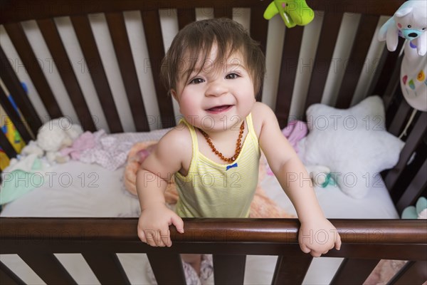 Mixed race baby girl standing in crib