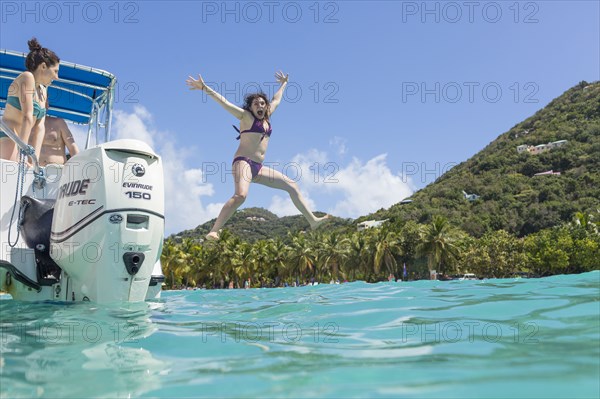 Caucasian woman jumping off boat in tropical ocean