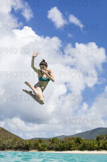 Caucasian woman jumping into tropical ocean